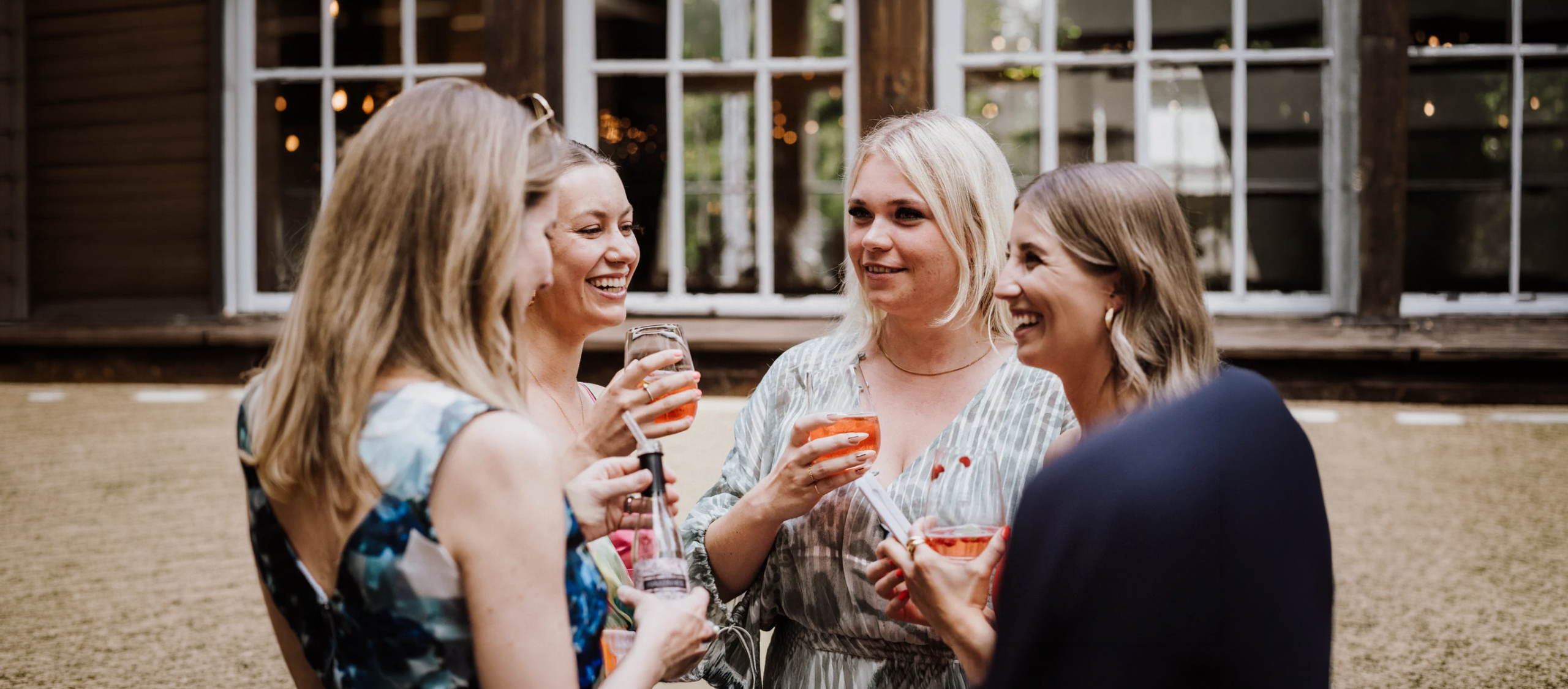 Vier Frauen lachen und trinken gemeinsam bei Feier im Außenbereich
