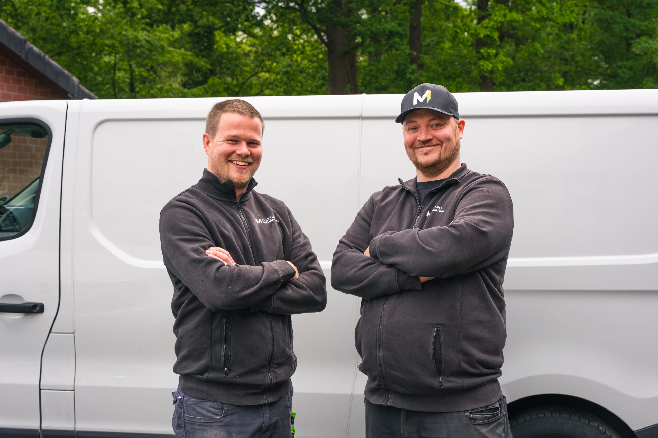 Zwei Mitarbeiter von Elektro Mersmann in Arbeitskleidung vor dem Firmenfahrzeug in Harsewinkel